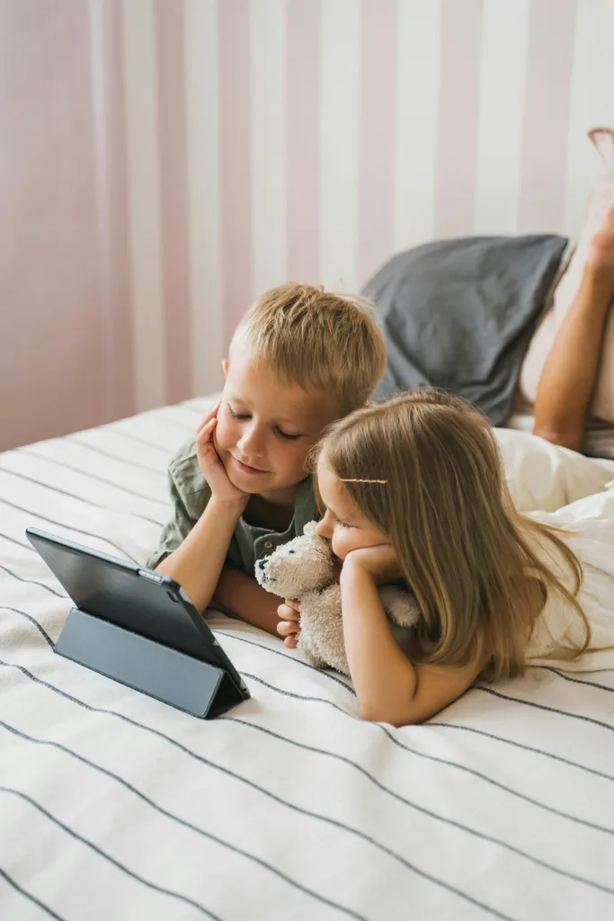 Two children watching a tablet together on a bed