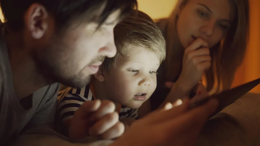 A child using a tablet while a parent controls the setup